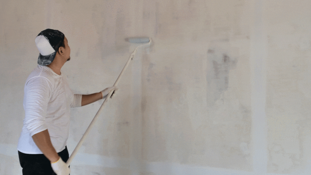 A man painting over a plastered wall.